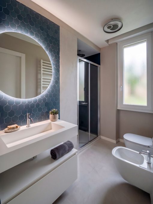 Bagno padronale con specchio retroilluminato e piastrelle a squama blu